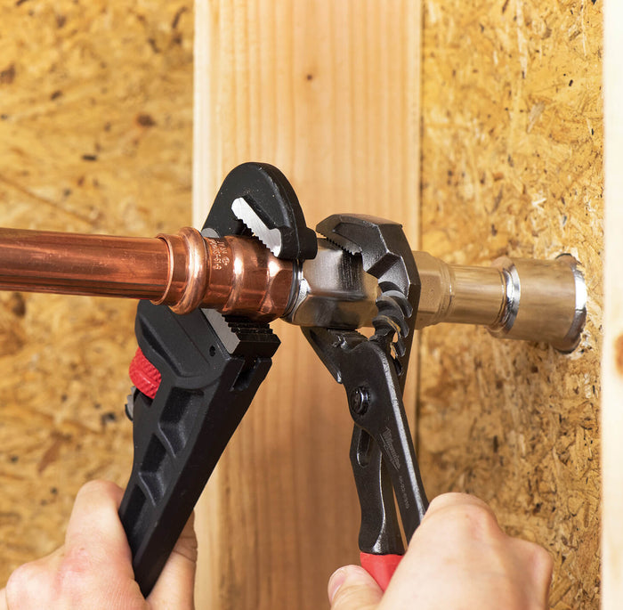 Two hands tightening the connections between the three-quarters inch NPT inlet and copper pipe plumbing with two wrenches.