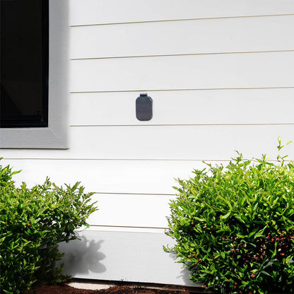 A slate gray house hydrant v2+ with the cover closed on the white lap siding of a home.