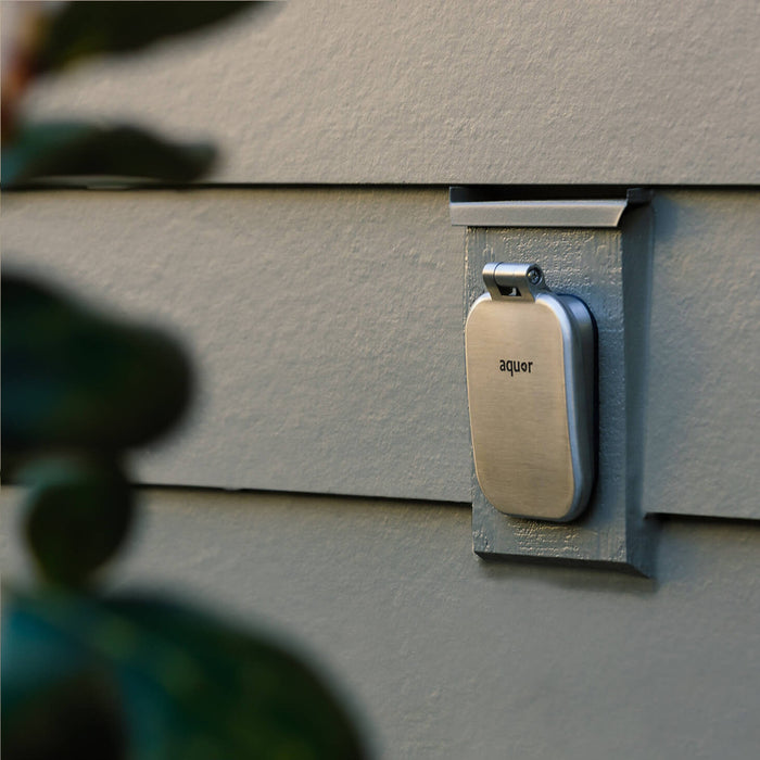 A brushed stainless v2+ debris cover shown on gray lap siding.|47730985795834